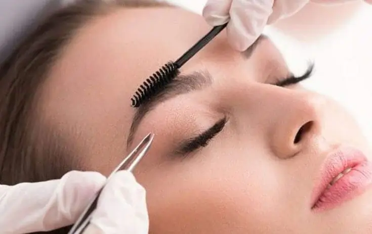 Uma profissional usando uma pinça para modelar a sobrancelha de uma cliente, representando o kit para iniciantes.